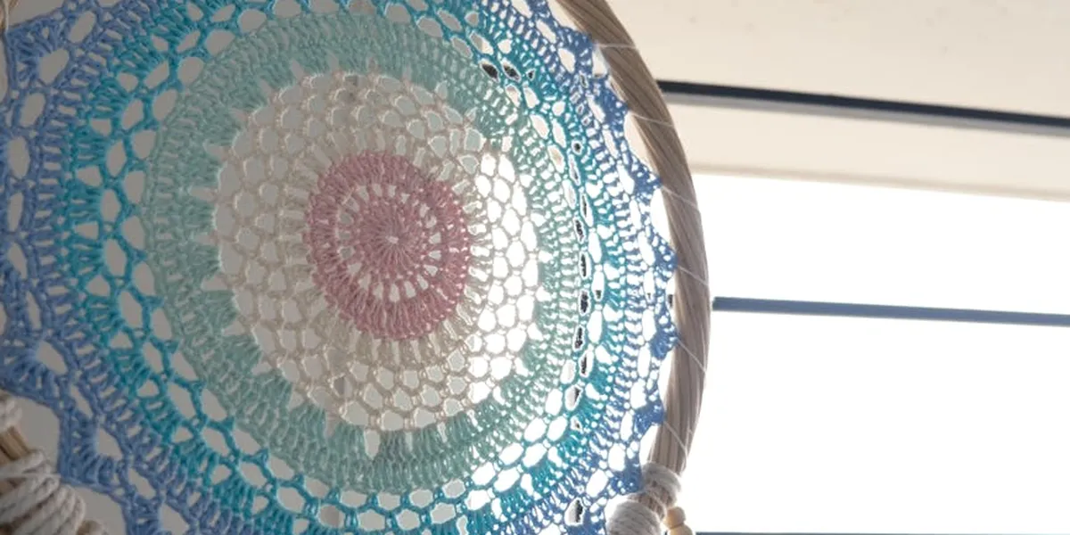 Close-up of a circular crocheted doily in pastel blue, green, and pink, arranged like a mandala