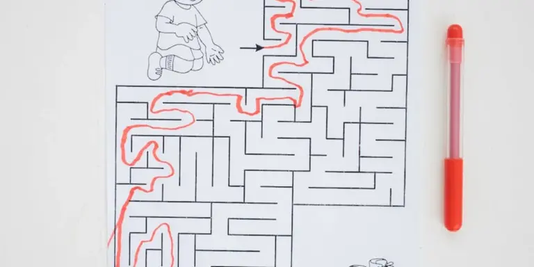 Black-and-white maze with a red path tracing a route; a small cartoon figure sits at the top, and a red marker lies to the right.