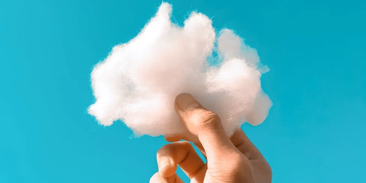 A hand holding a fluffy white cloud against a clear blue sky.