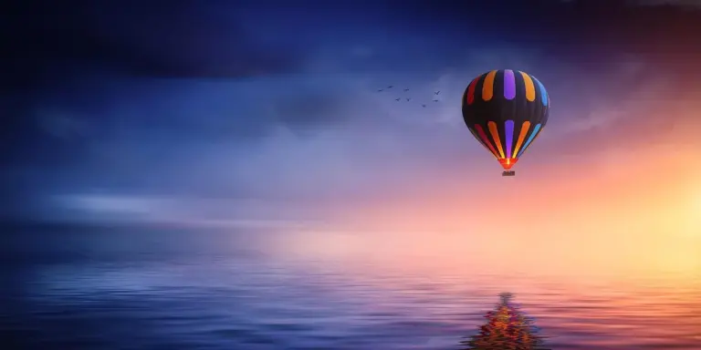 Colorful hot air balloon floating over a calm ocean at sunset, with a gradient sky from blue to warm orange, evoking dreamlike imagery.