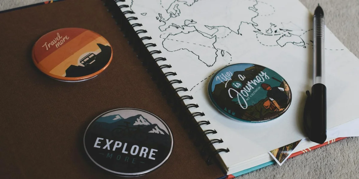 Close-up of a notebook with a world map, a pen, and three circular buttons with travel-themed labels, suggesting exploration of dreams.
