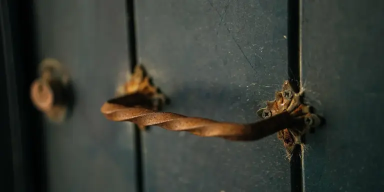 Close-up of a weathered blue door with a twisted brown rope threaded through a metal latch, evoking entrapment.