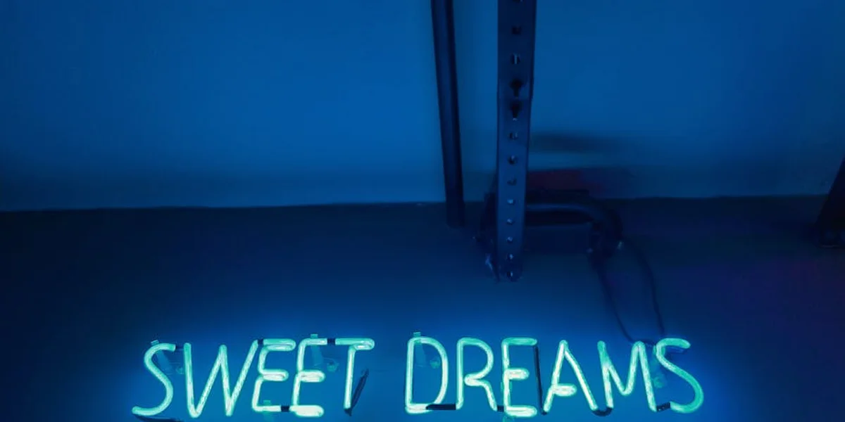 Blue neon 'SWEET DREAMS' sign glowing in a dark blue space, suggesting hidden or unheard messages within dreams.