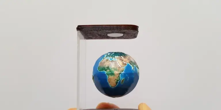 Small globe of the Earth suspended in a clear display case with a wooden top, set against a pale background.