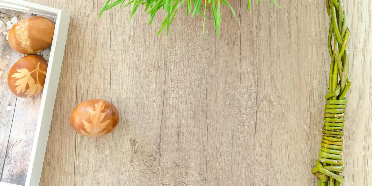 Brown eggs with decorative patterns in a white tray on a wooden surface, with green plants in the background