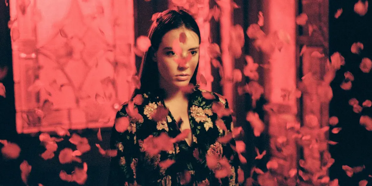 A contemplative woman surrounded by drifting pink petals in a dreamlike setting.