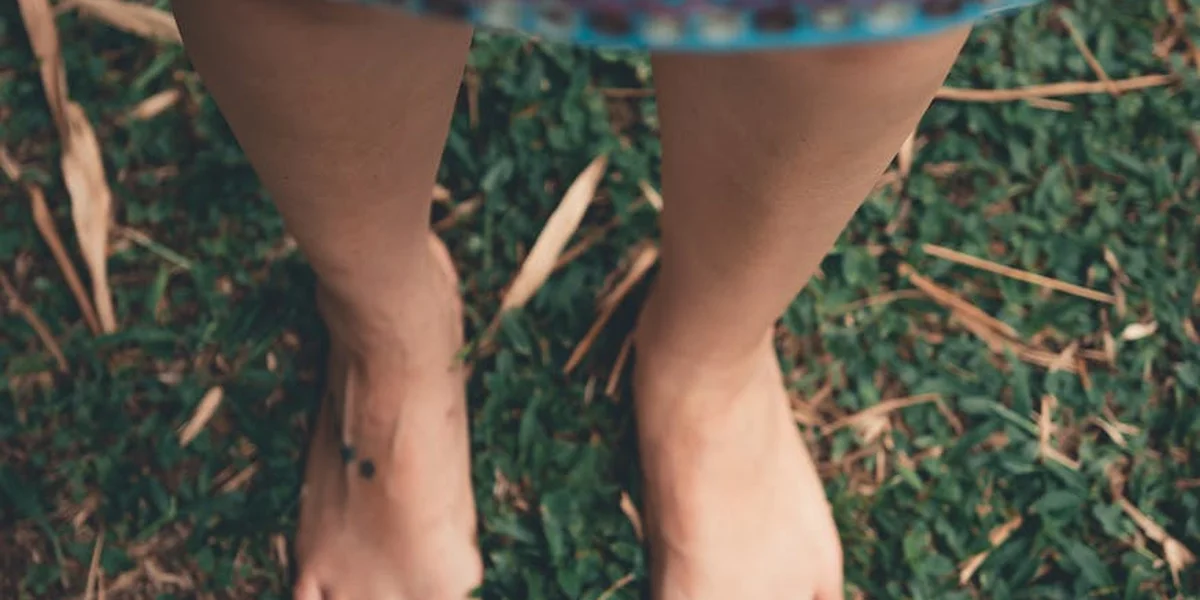 Bare feet and lower legs standing on green grass with scattered leaves