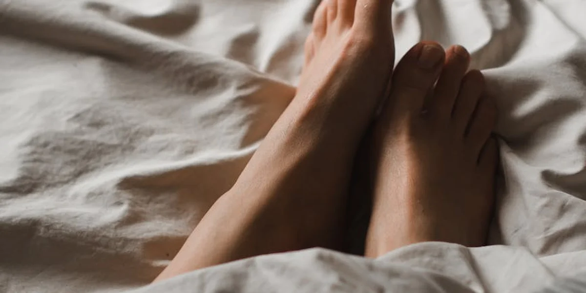 Close-up of bare feet resting on a rumpled white bed sheet