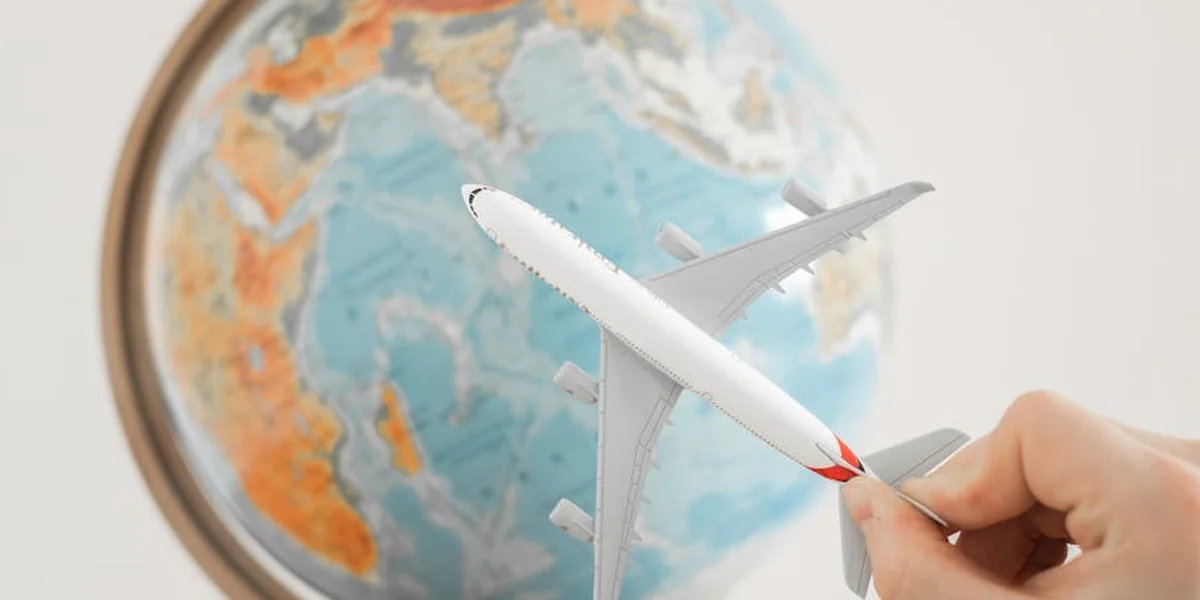 Globe with a white paper airplane hovering above, held by a hand, suggesting a dreamlike journey
