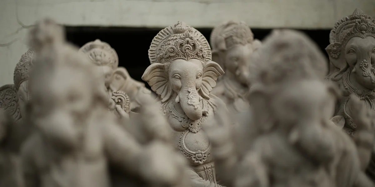Close-up of carved stone statues of Lord Ganesha in a row, with the central figure in sharp focus and others blurred in the foreground.