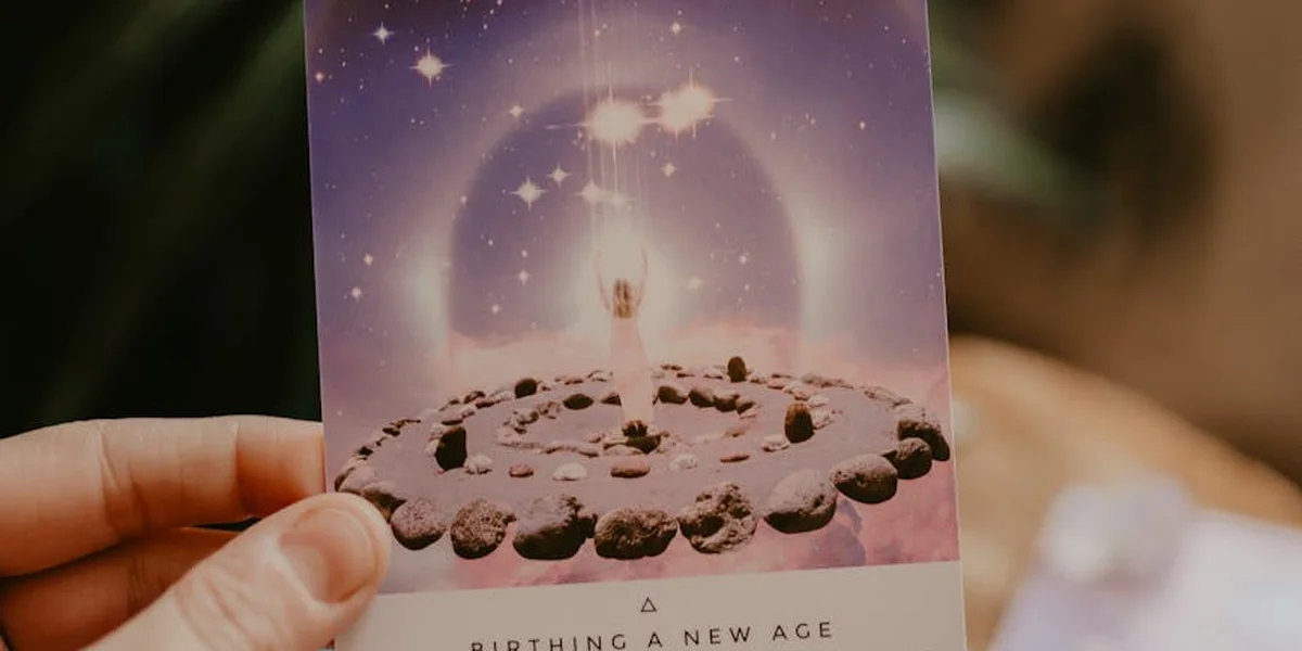 A hand holds a card with a purple glow and a ring of small stones arranged in a circle, with stars and a luminous aura in the background.