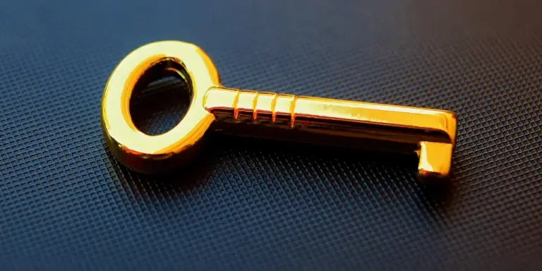Close-up of a shiny gold key resting on a dark textured surface.