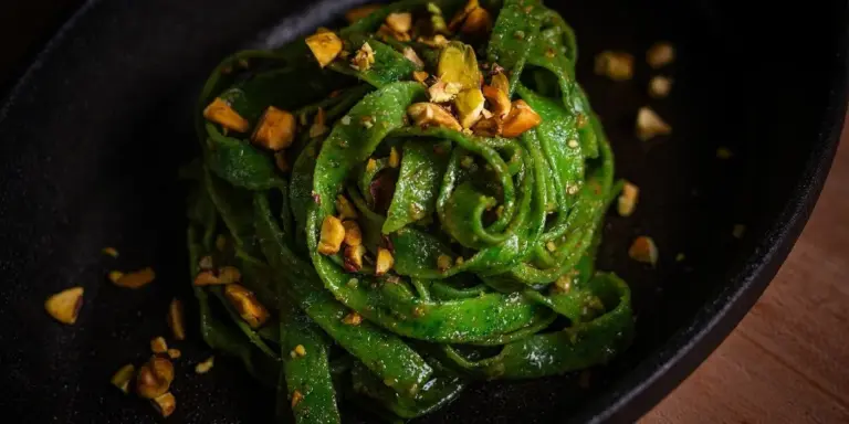 Spinach-green pasta with chopped nuts on a dark plate