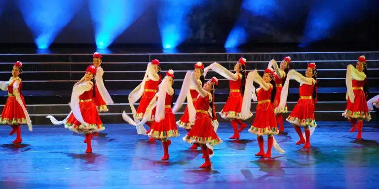 Group of dancers in red dresses performing a choreographed routine on a stage with blue lighting