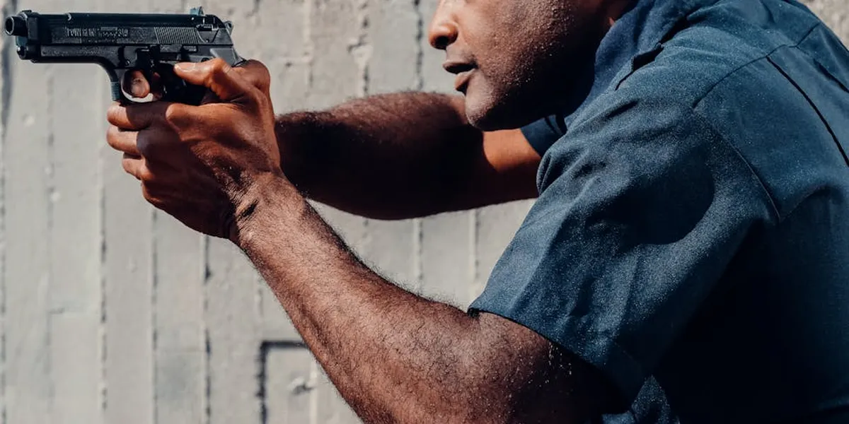 Man wearing a dark blue shirt aiming a handgun in a tense, focused posture.