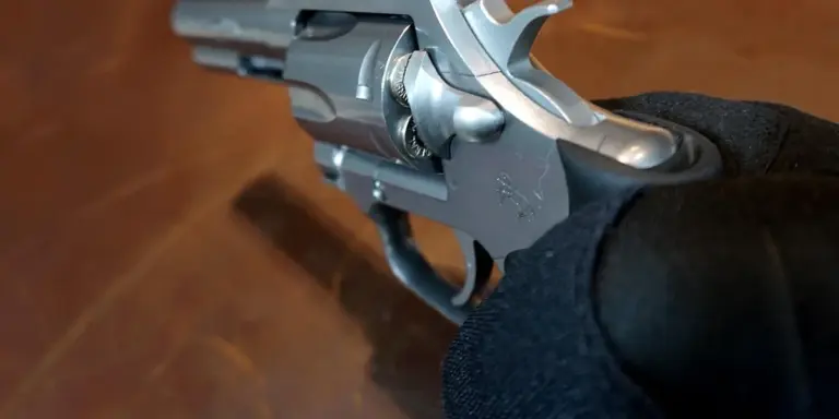 Close-up of a silver revolver held by a gloved hand above a wooden surface.