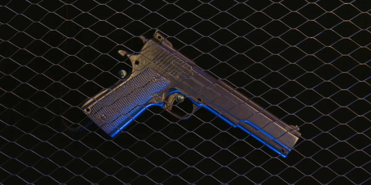 Handgun pressed against a chain-link fence, symbolizing threat, danger, and boundaries in dreams.
