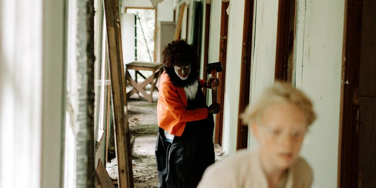 Dim, narrow hallway with a blurred foreground figure and a person in an orange top in the background, conveying confusion and unease.