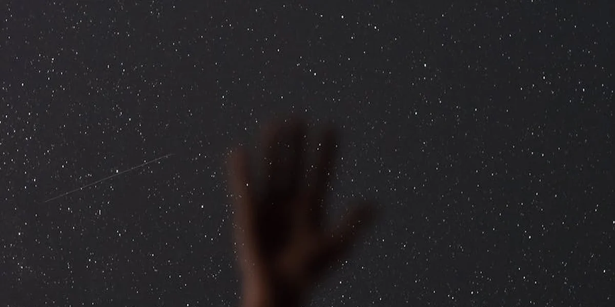 Blurred silhouette of a hand reaching toward a star-filled night sky.