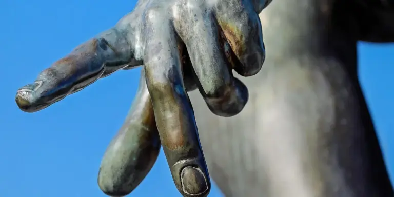 Bronze statue hand pointing forward against a blue sky.