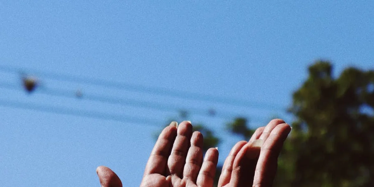 Close-up of multiple hands held together in front of a clear blue sky, symbolizing body-part dream symbolism.