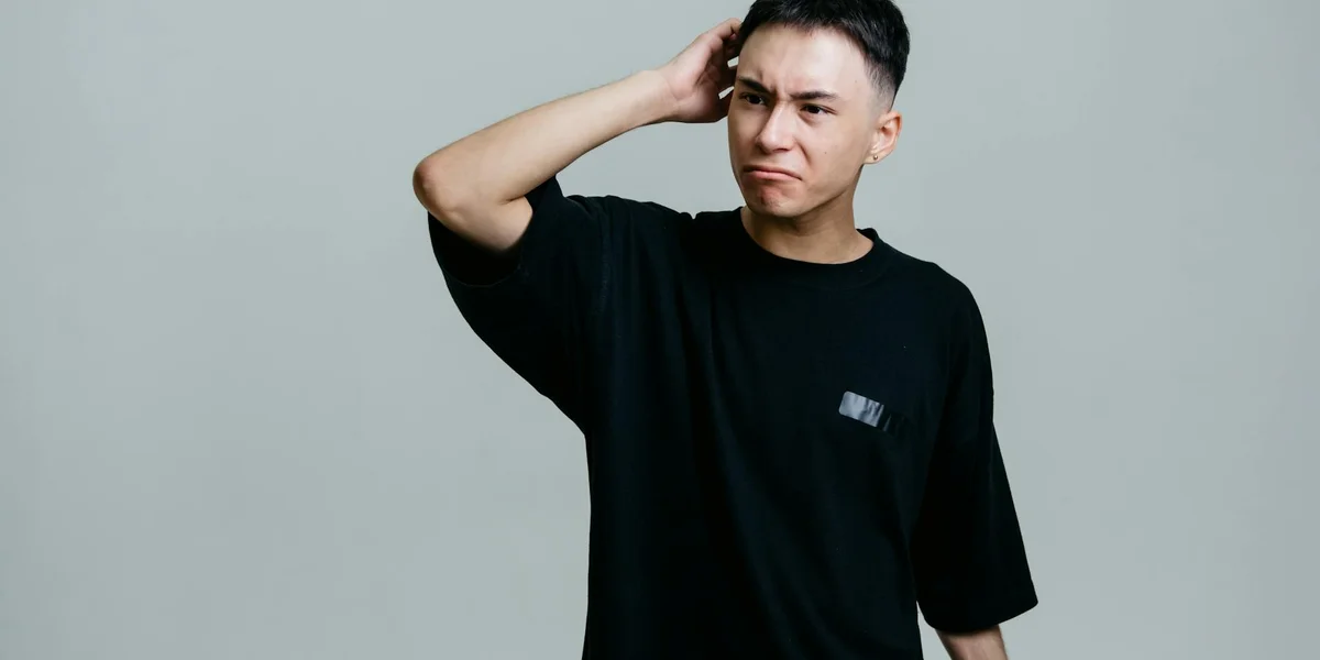 Person scratching their head in a black shirt, looking puzzled or concerned.
