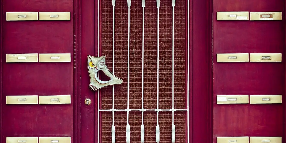 A bright pink front door featuring a metal grate with vertical bars in the middle and rows of beige mail slots along both sides.