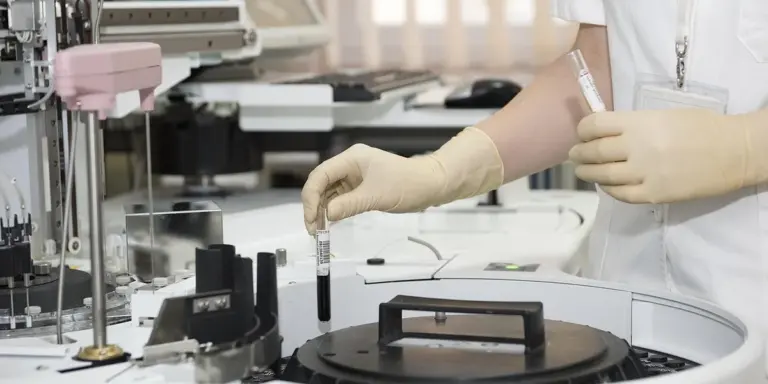 A healthcare worker wearing gloves handles a test tube in a medical laboratory.
