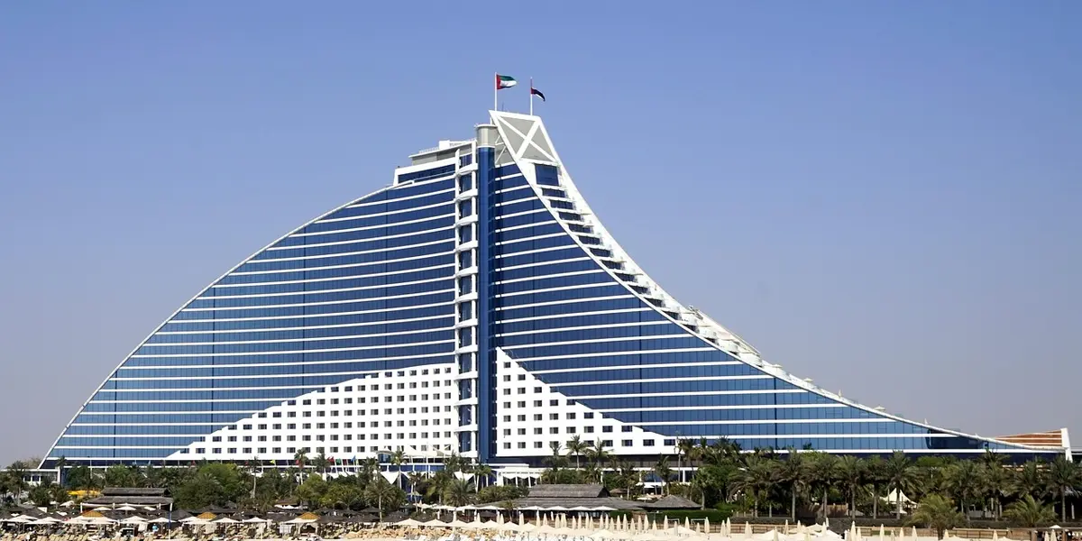 Sail-shaped luxury hotel along a coastline under a clear blue sky