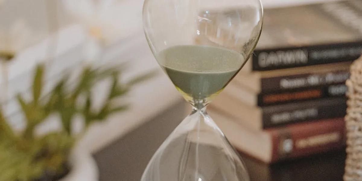 An hourglass on a desk with a stack of books in the background, symbolizing time distortion in dreams.