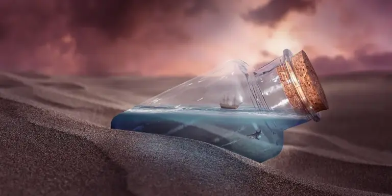 A glass bottle with a cork lies partially buried in sunlit desert sand with a pink sunset sky.