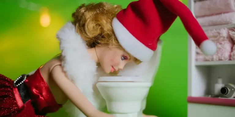 A person wearing a Santa hat and red outfit leaning over a toilet in a bright green room.