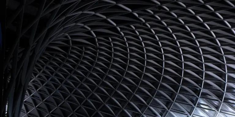 Close-up of a dark, interwoven lattice of curved beams forming a repetitive geometric pattern, evoking an impossible architectural interior.