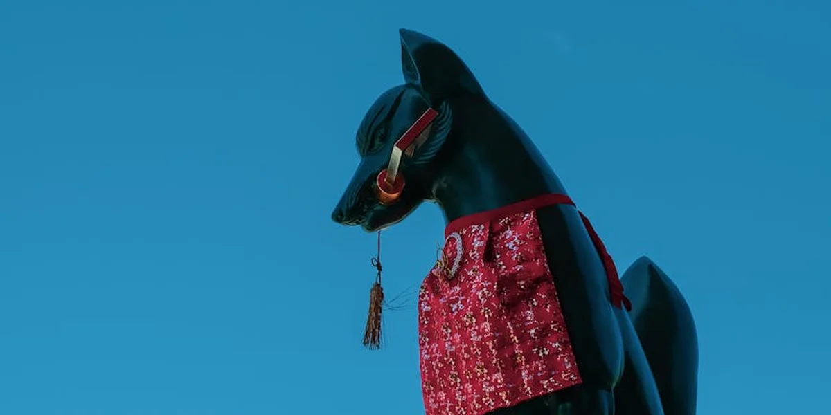 Black fox statue (kitsune) wearing a red bib, set against a clear blue sky.