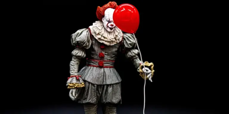 An eerie clown in period costume holding a red balloon against a dark background.