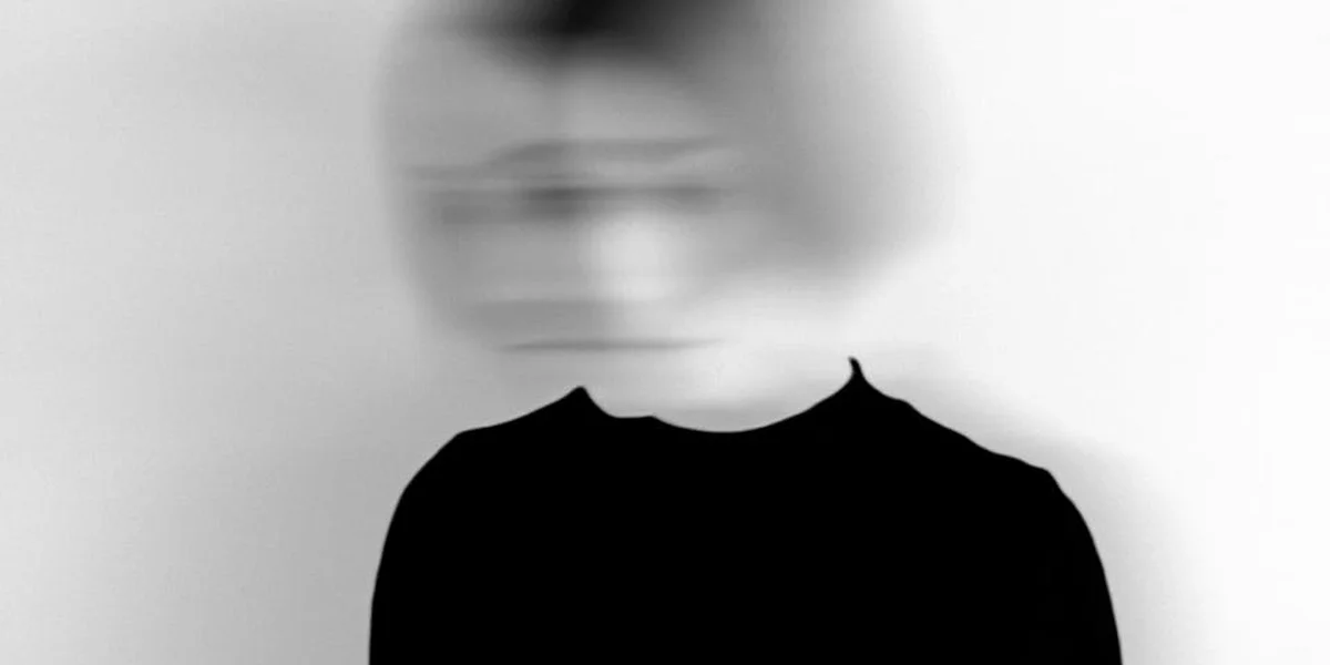 Blurred silhouette of a person in a black top against a pale background, suggesting dreamlike uncertainty.