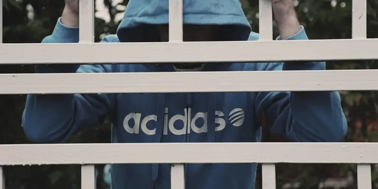 Person behind bars in a blue hoodie, suggesting confinement or imprisonment.