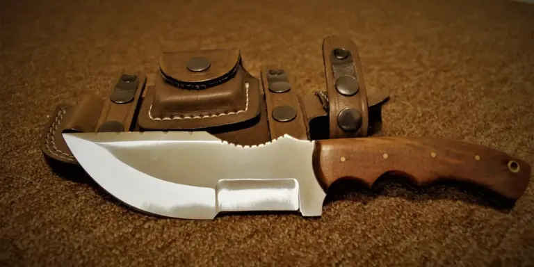 A fixed-blade knife with a wooden handle and brown leather sheath resting on a carpet.