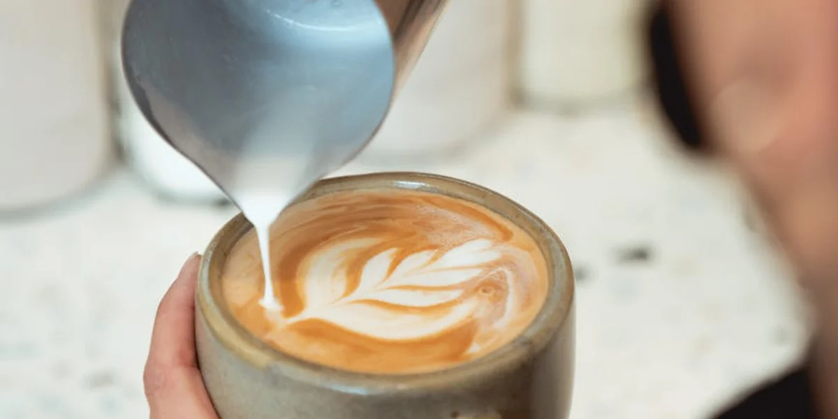 Close-up of a barista pouring steamed milk to create latte art in a cup.