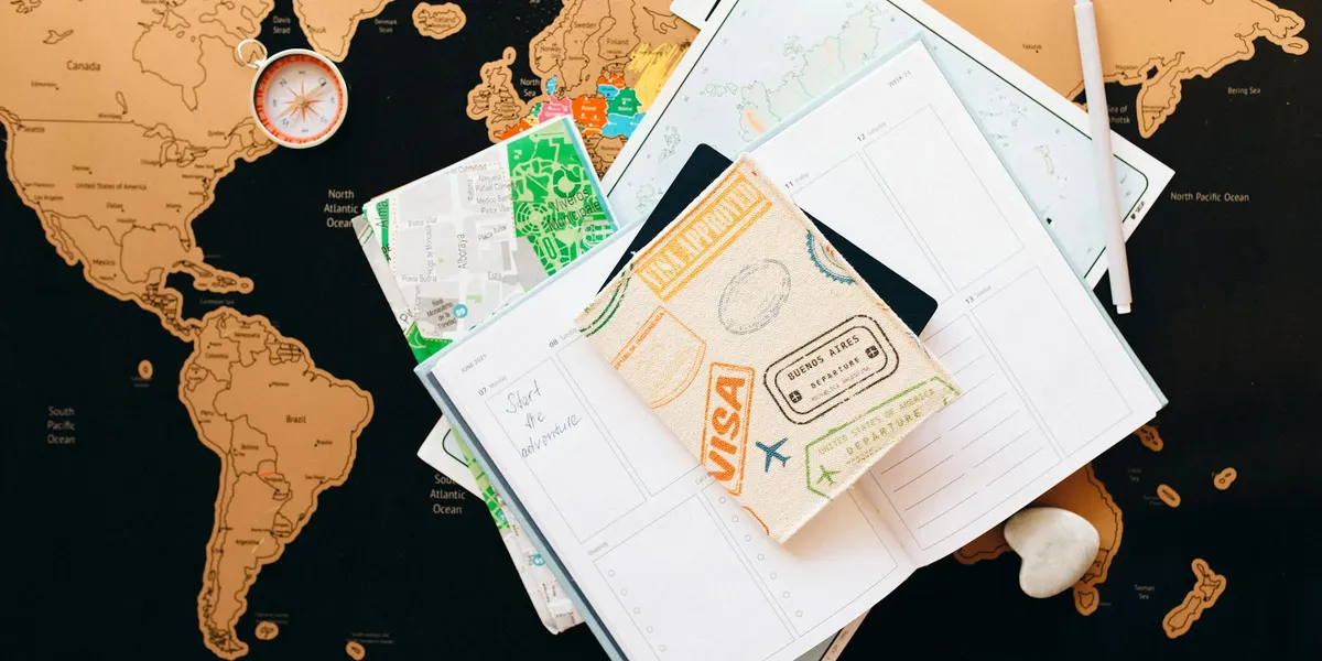 Overhead collage of travel paperwork on a world map: scattered maps, a passport, boarding passes, and a small compass.