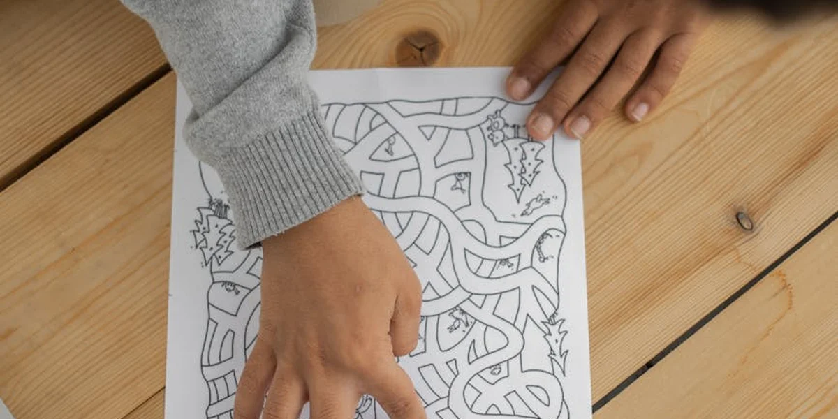 Close-up of hands tracing a path through a maze on a piece of paper placed on a wooden table, symbolizing navigation from confusion to clarity.