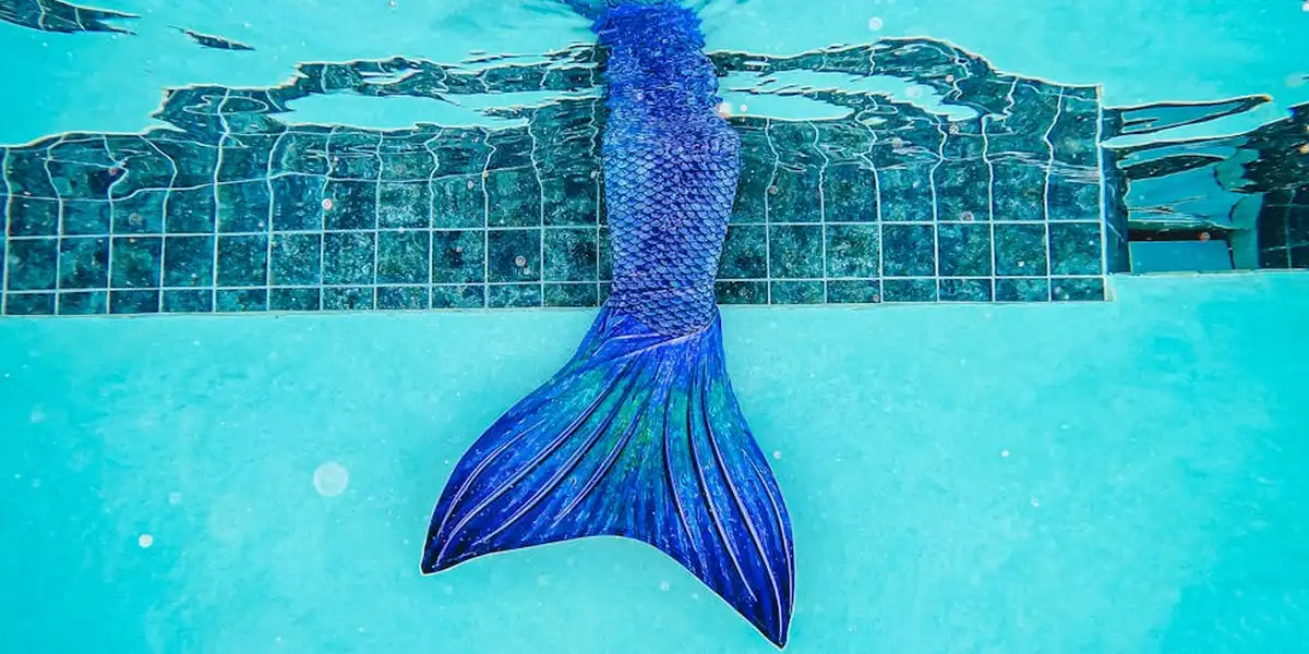 Underwater view of a blue mermaid tail beside a tiled pool edge