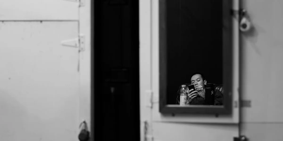 Black-and-white photograph of a person reflected in a wall-mounted mirror, embodying introspection.