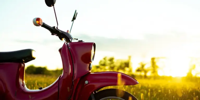 A red vintage motorcycle bathed in golden sunset light in a grassy field