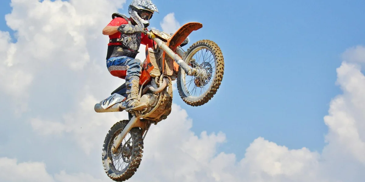 Motocross rider in mid-air on an orange dirt bike against a blue sky.