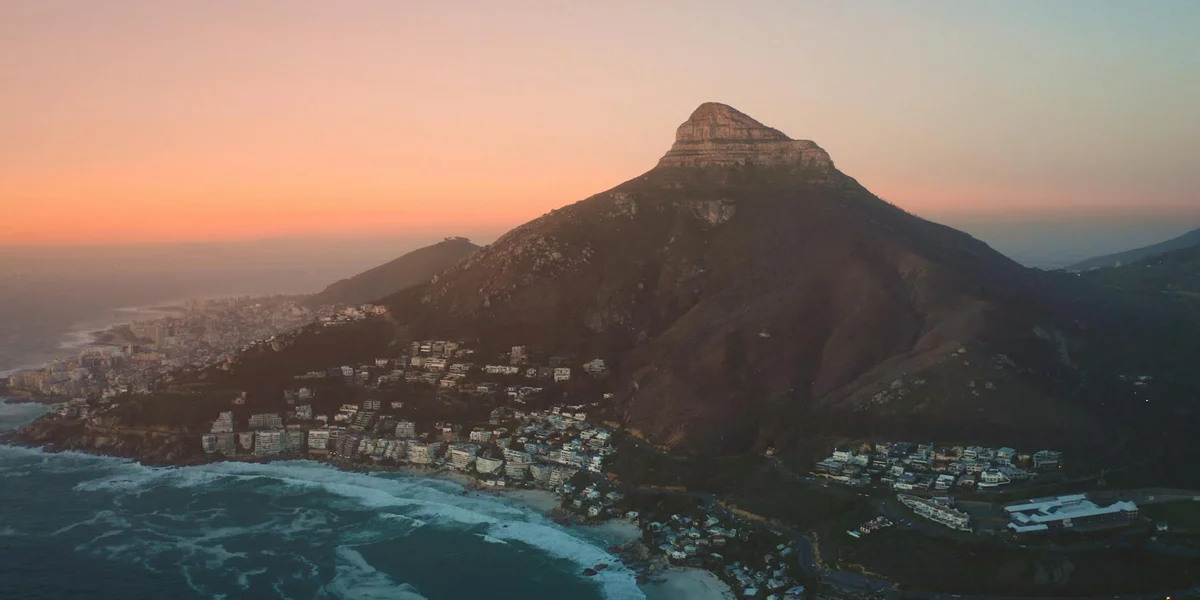 Coastal town at sunset with a prominent mountain peak in the foreground.