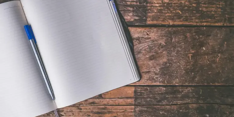 Open notebook with a blue pen on a textured wooden table, suggesting journaling or planning after waking from a nightmare.
