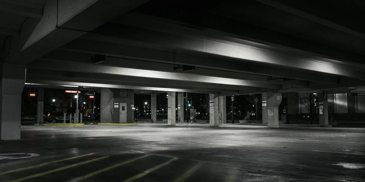 Empty, dimly lit multi-level parking garage with concrete pillars and long shadows under overhead beams.