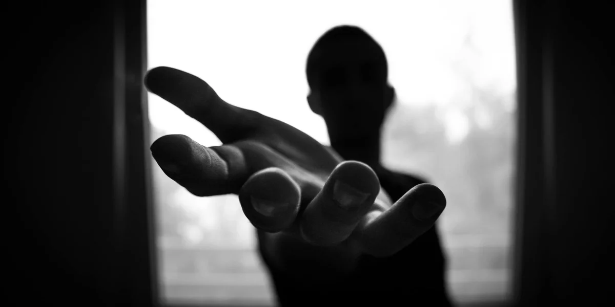 A black-and-white silhouette of a person reaching forward with an open hand, suggesting healing energy being offered.