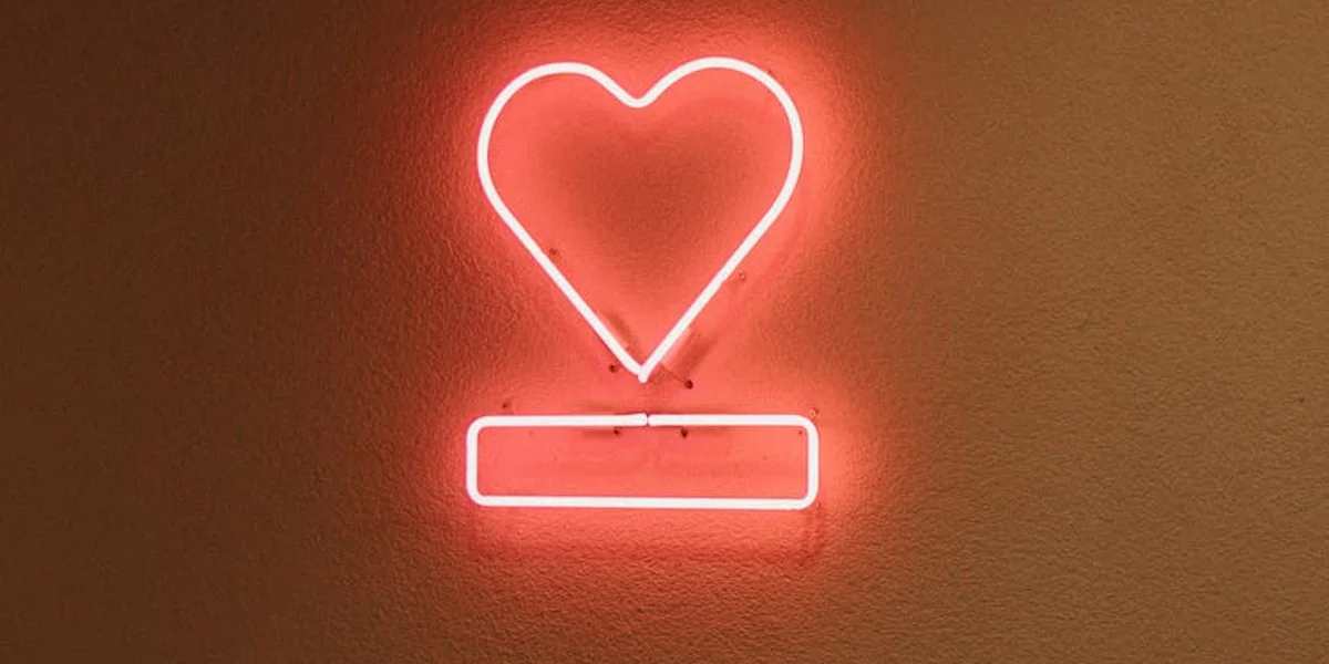 A glowing pink neon heart above a rectangular glow on a textured wall, symbolizing love, compassion, and the heart chakra in dreams.
